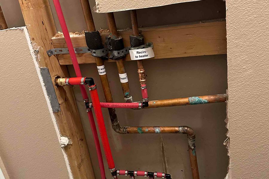 Exposed wall showing copper and red PEX plumbing with labels