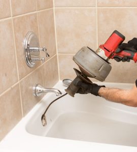 Benjamin Franklin plumber using a power drain auger to unclog a bathtub drain.