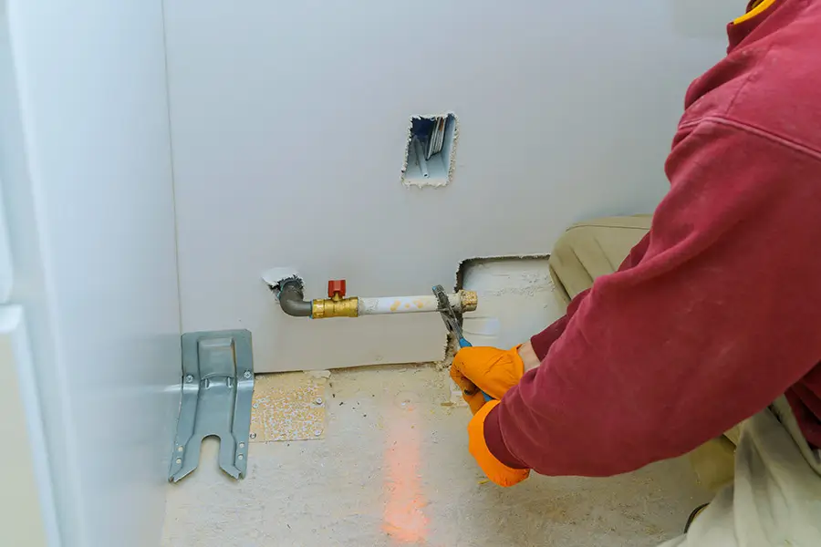 Worker in orange gloves repairing a gas line near a white wall